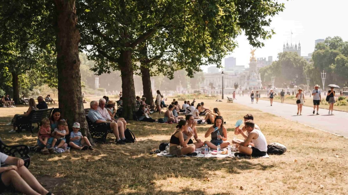 People walking through a dry, sun-baked park in London during the 2026 summer heatwave.