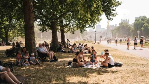 People walking through a dry, sun-baked park in London during the 2026 summer heatwave.